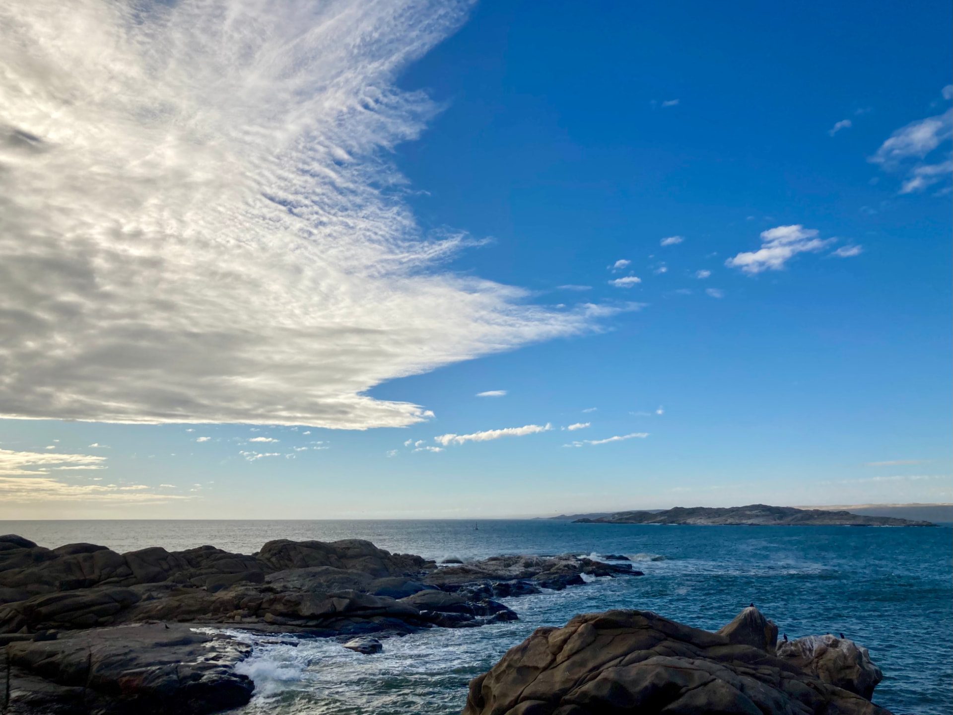 Rocky Atlantic coastline near Lüderitz with waves breaking on boulders and a vast blue sky