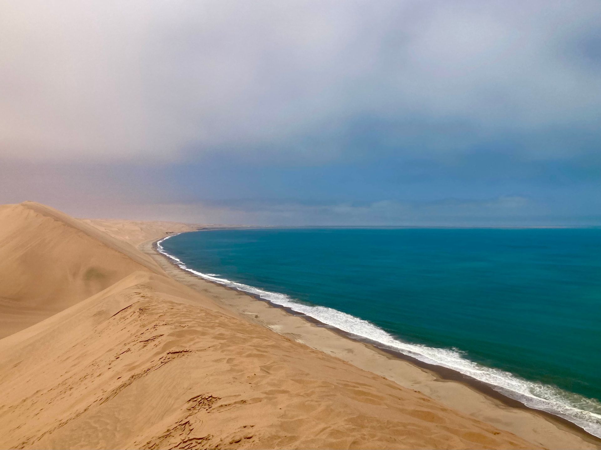 Towering sand dunes meeting the turquoise Atlantic in a long curving shoreline at Sandwich Harbour