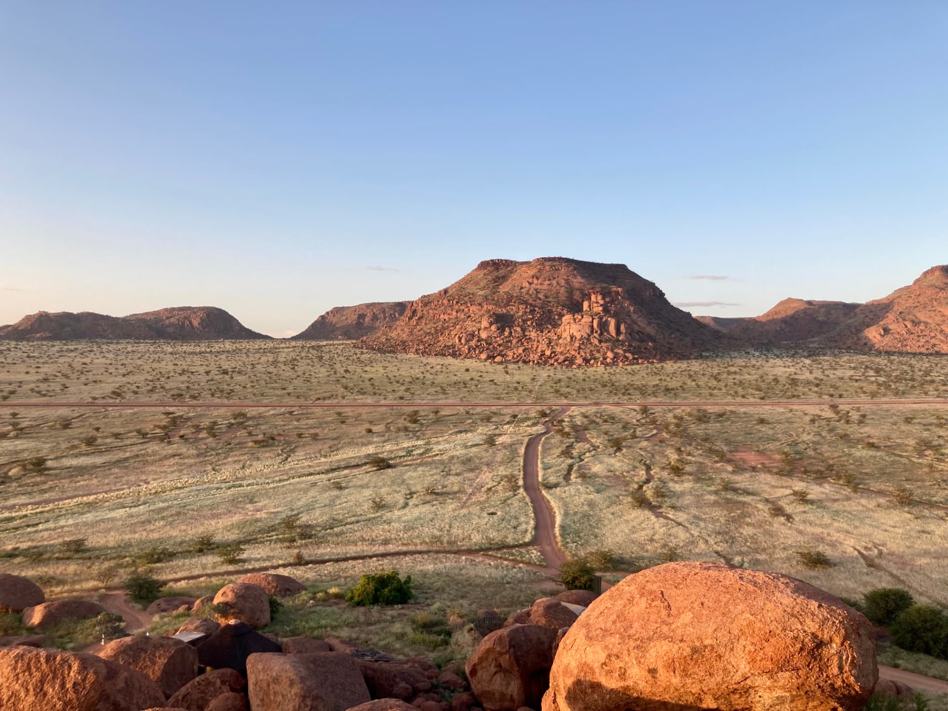 Granite boulders and open grassland below flat-topped Damaraland hills glowing in low sunlight