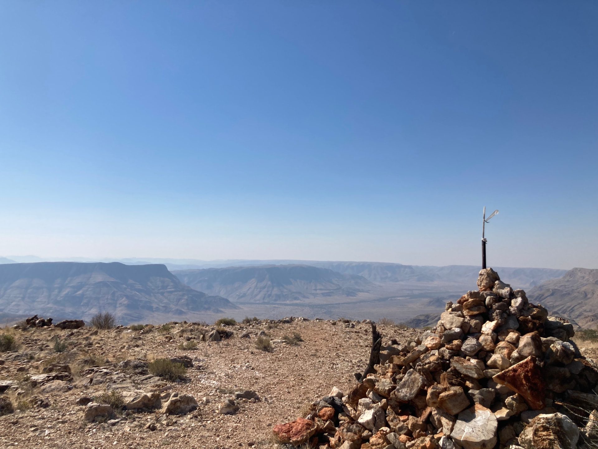 A stone cairn on a rocky ridge above a hazy layered canyon landscape