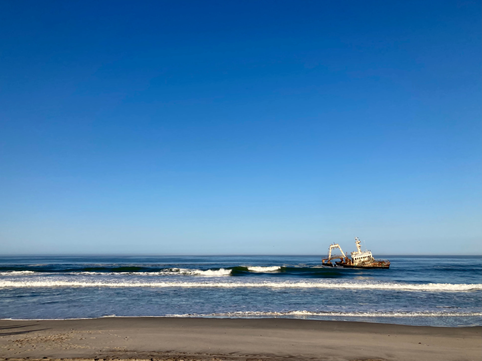 A rusting shipwreck in the surf off the Skeleton Coast under a clear blue sky