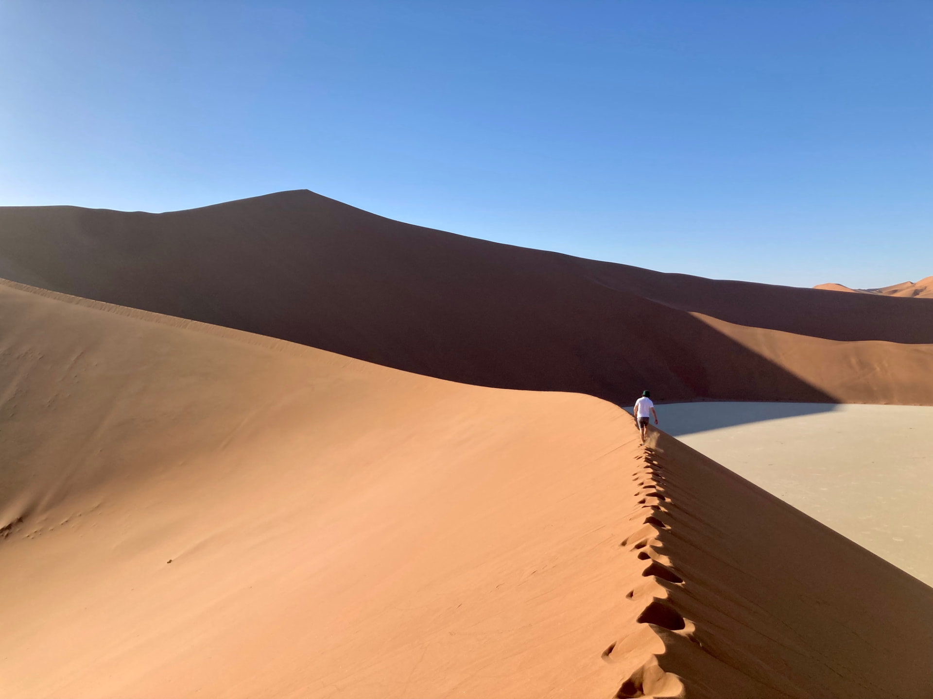 A single walker following the crest of a tall red dune above a white pan