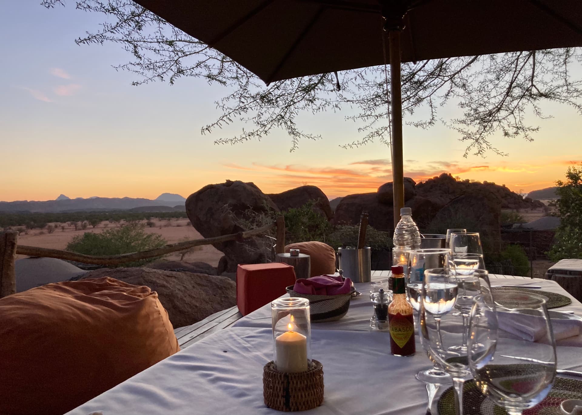 A candlelit table set with wine glasses at a desert lodge at dusk