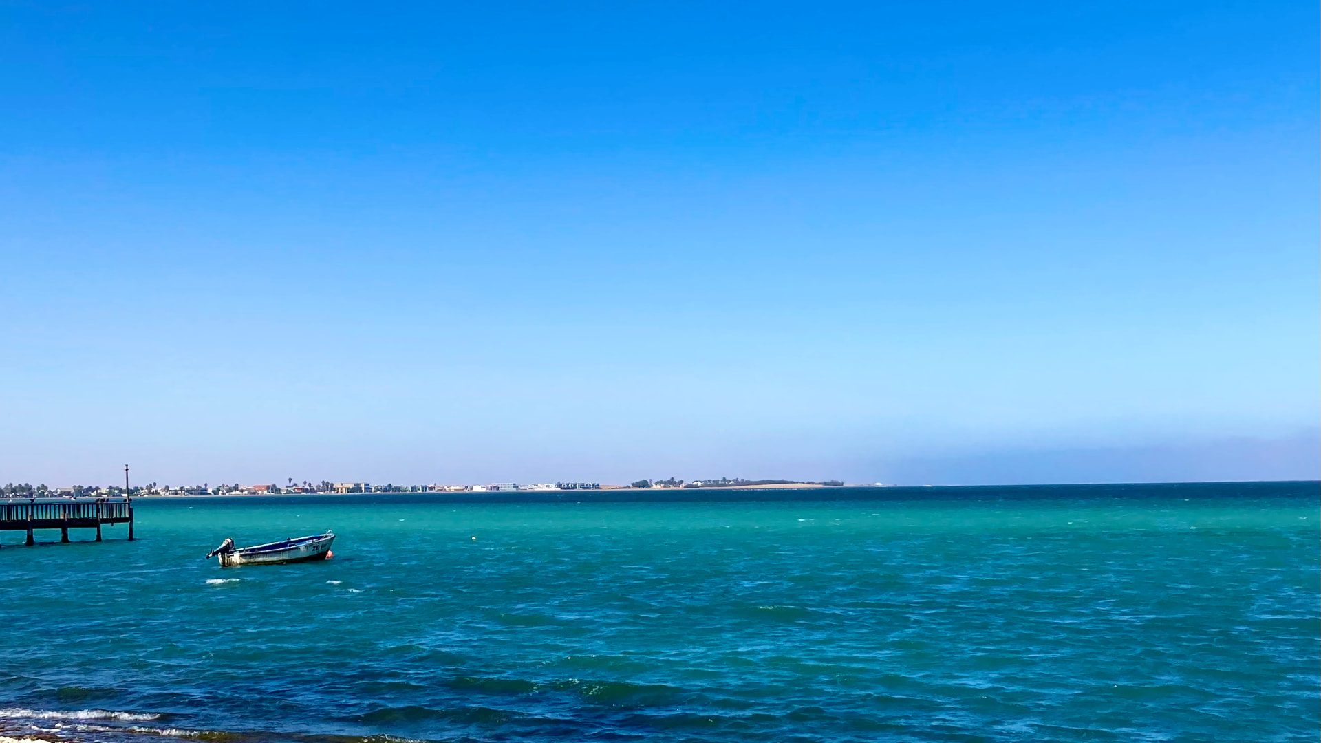 A small boat moored in turquoise water off a jetty on the Namibian coast