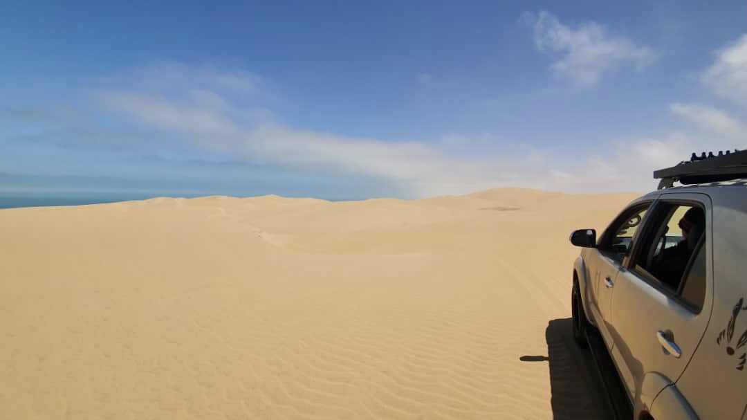 A 4x4 pausing on soft coastal dunes with the Atlantic just visible beyond