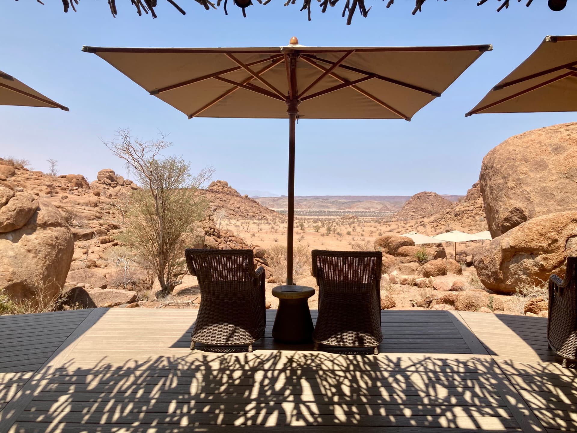 Shaded lodge deck chairs under umbrellas looking out over Damaraland's granite boulders