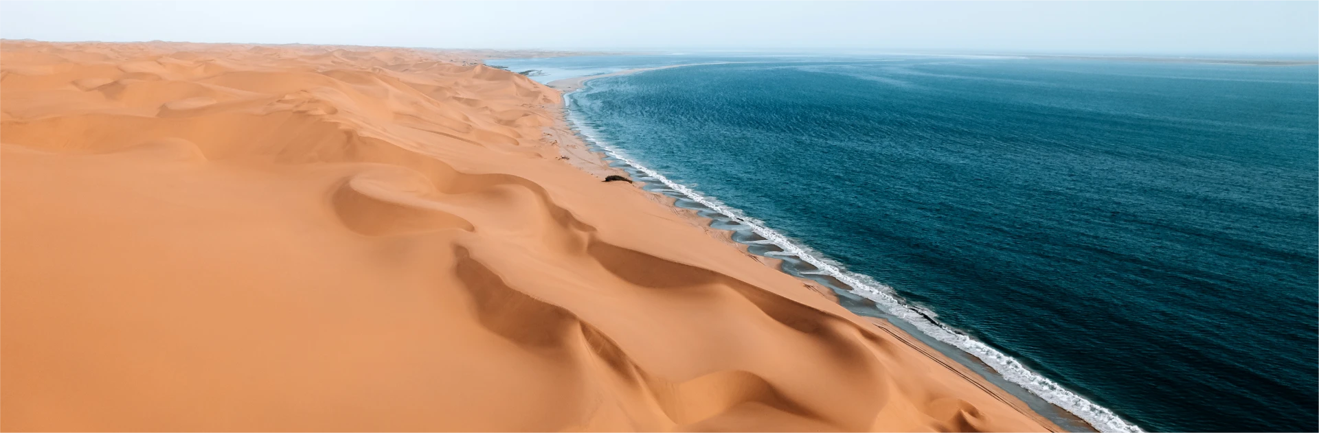 Orange Namibian sand dunes meeting the turquoise Atlantic coastline from above