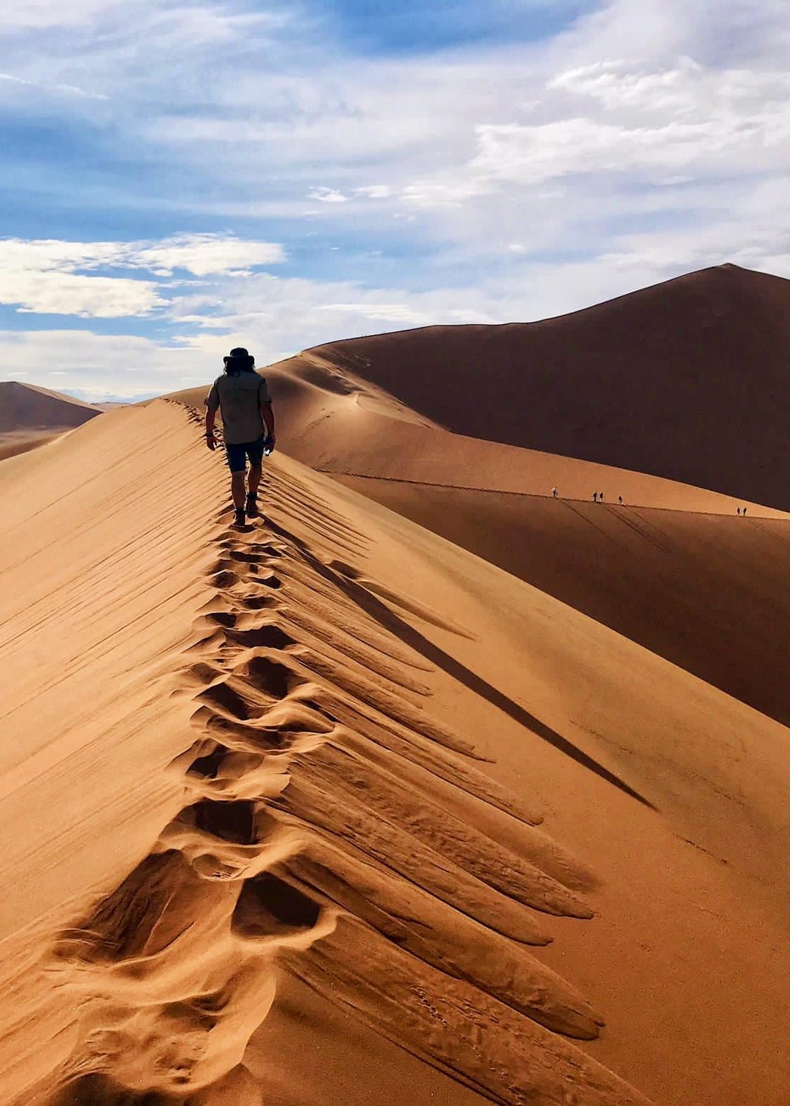 A walker climbing the ridge of a towering dune, footprints trailing behind